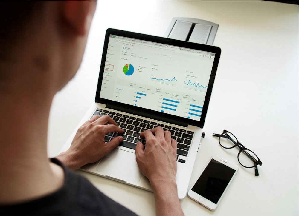 Pessoa de costas trabalhando em um notebook com painel de gráficos