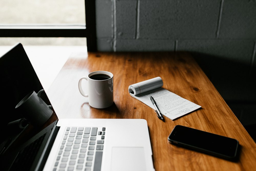 Mesa de trabalho organizada com notebook, caneca de café e bloco de anotações